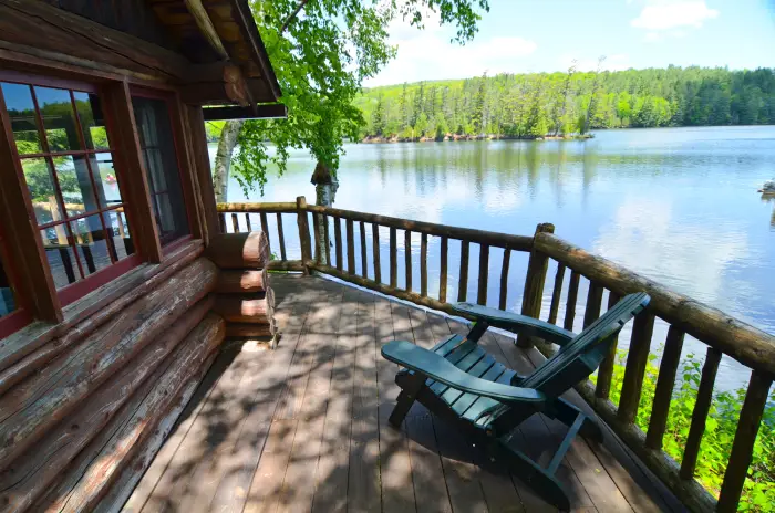 A rustic deck with an Adirondack chair looks out over a sparkling blue lake.