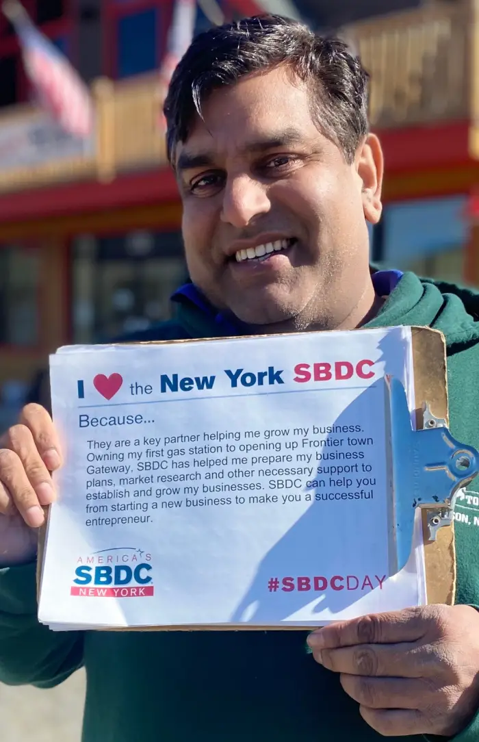 Muhammad &quot;Mo&quot; Ahmad smiles at the camera and holds a sign supporting small business.