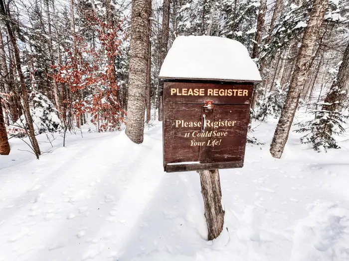 Deep snow around a brown box trail register&#44; piled on top and high below.